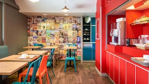 A cafe with wooden tables and colorful chairs, a wall of travel posters, and a red counter with a coffee machine. - hotelF1 Lyon Gerland Vénissieux (Venissieux)