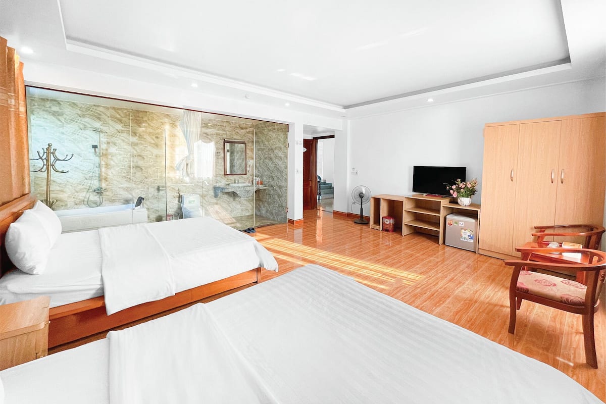 A modern hotel room with a large bed, a walk-in closet, a TV, and a bathroom with a glass shower enclosure.