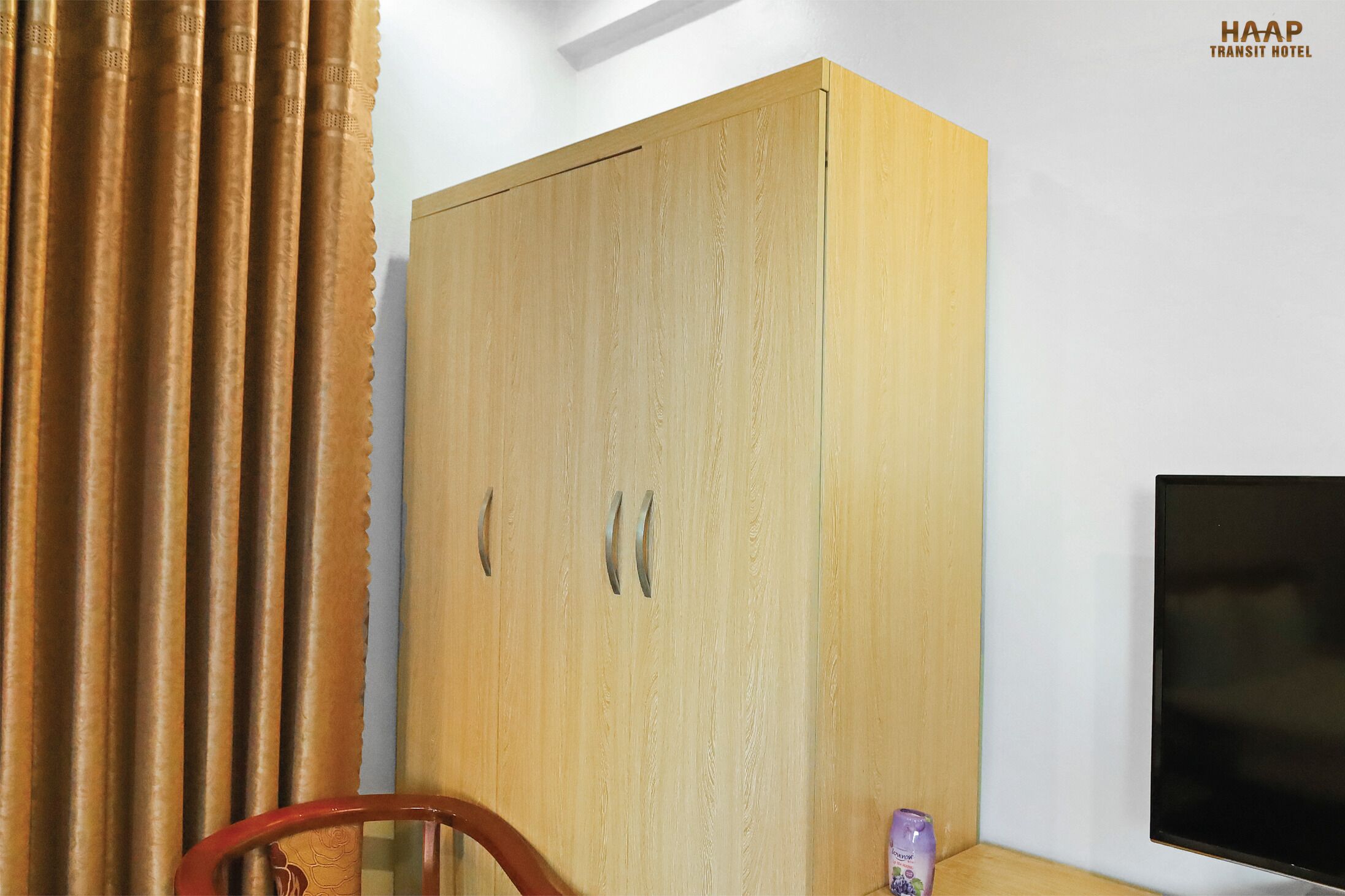 A wooden wardrobe with two handles, a television, and a curtain in a room.