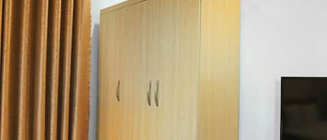 A wooden wardrobe with two handles, a television, and a curtain in a room.