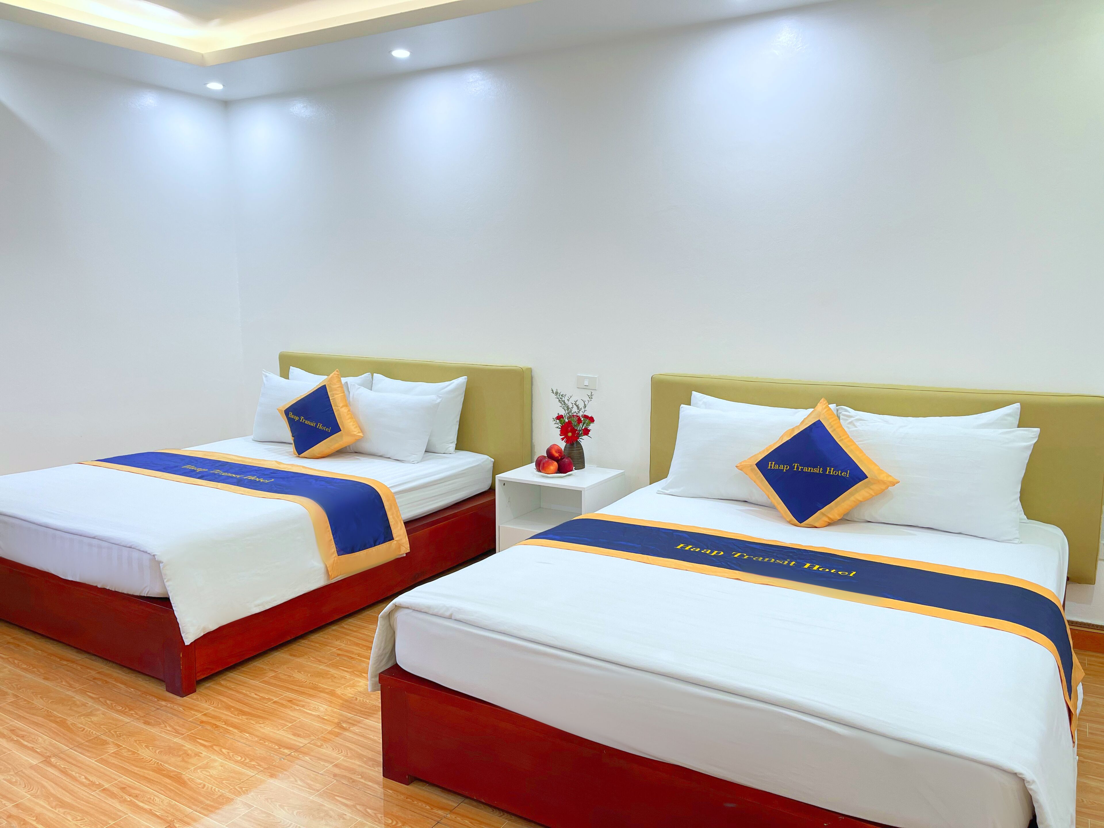 Habitación de hotel con dos camas, cada una con cabecera, ropa de cama blanca y correpasillos a rayas azules y amarillas.