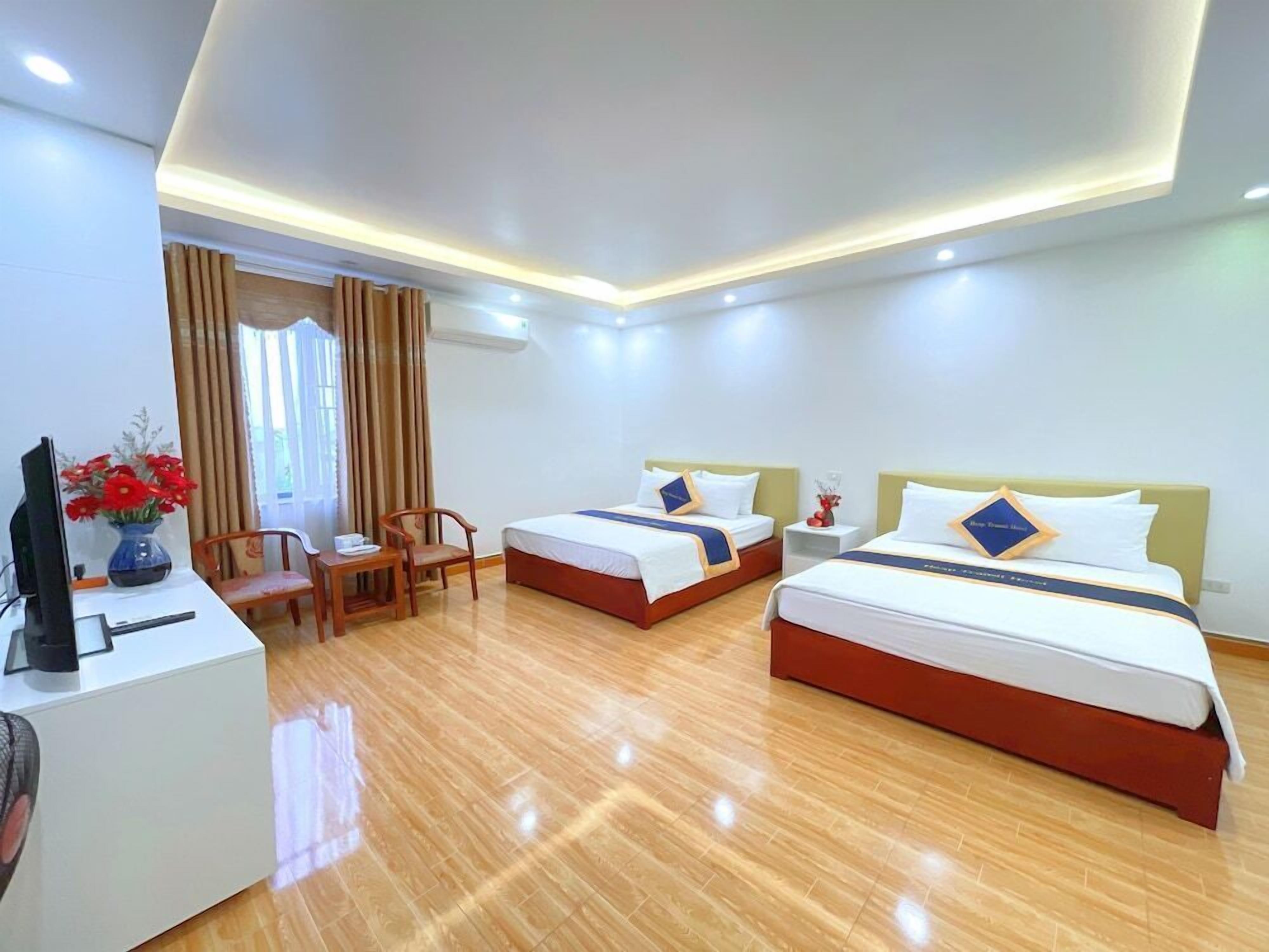 A hotel room with two beds, a desk, a chair, and a TV.