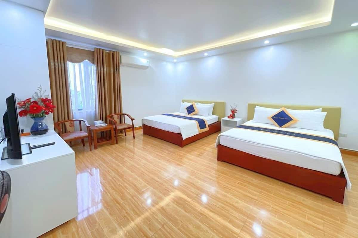 A hotel room with two beds, a desk, a chair, and a TV.