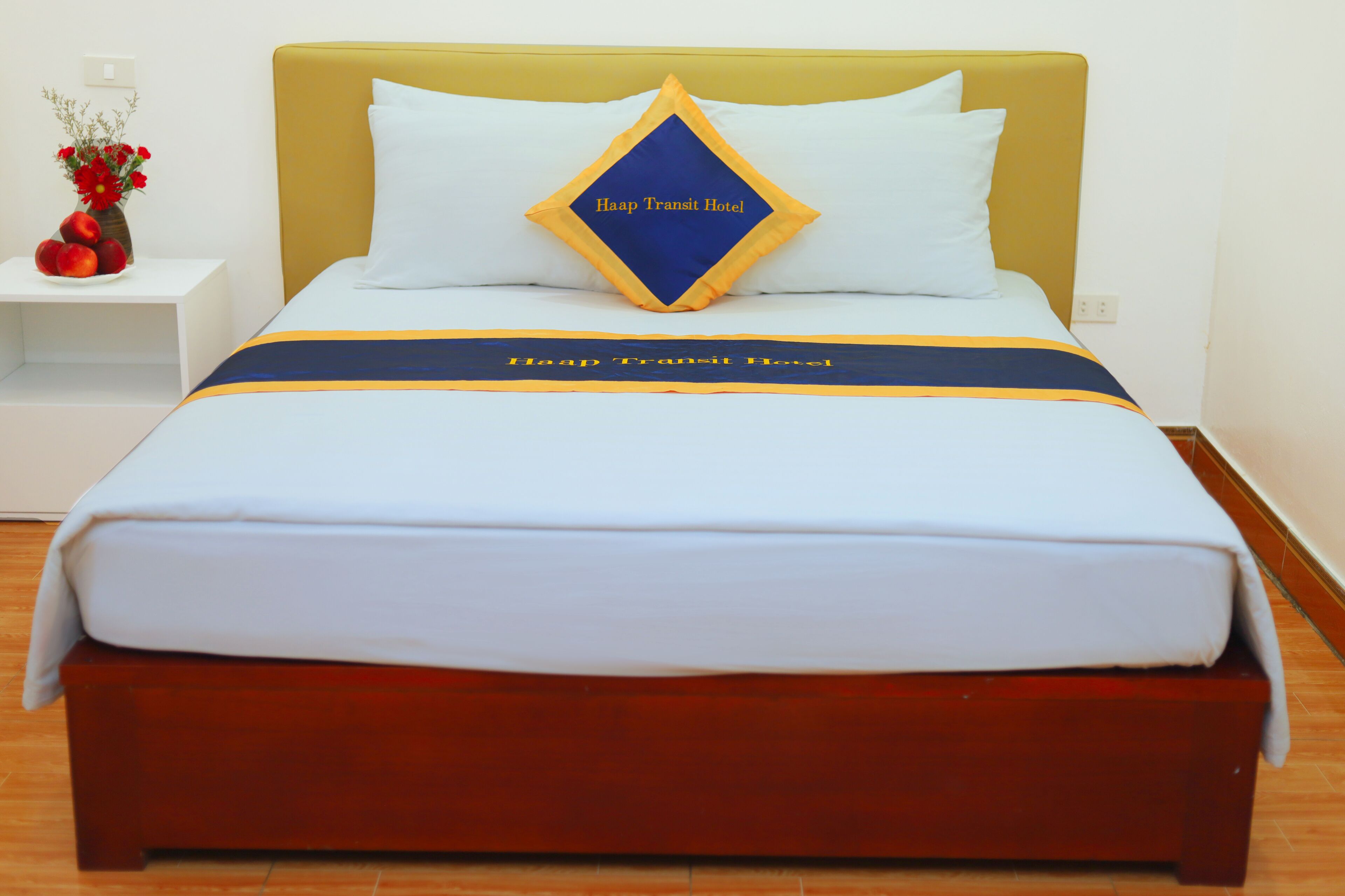 A bed with a yellow headboard, white bedding, and a blue and yellow striped bedspread.