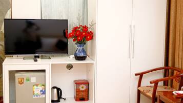Una habitación con una televisión sobre un mueble blanco, un jarrón con flores rojas, un farolillo rojo y una silla de madera.