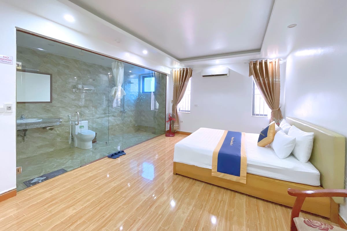 A hotel room with a glass-enclosed shower, a bed with a blue and white bedspread, and a wooden floor.