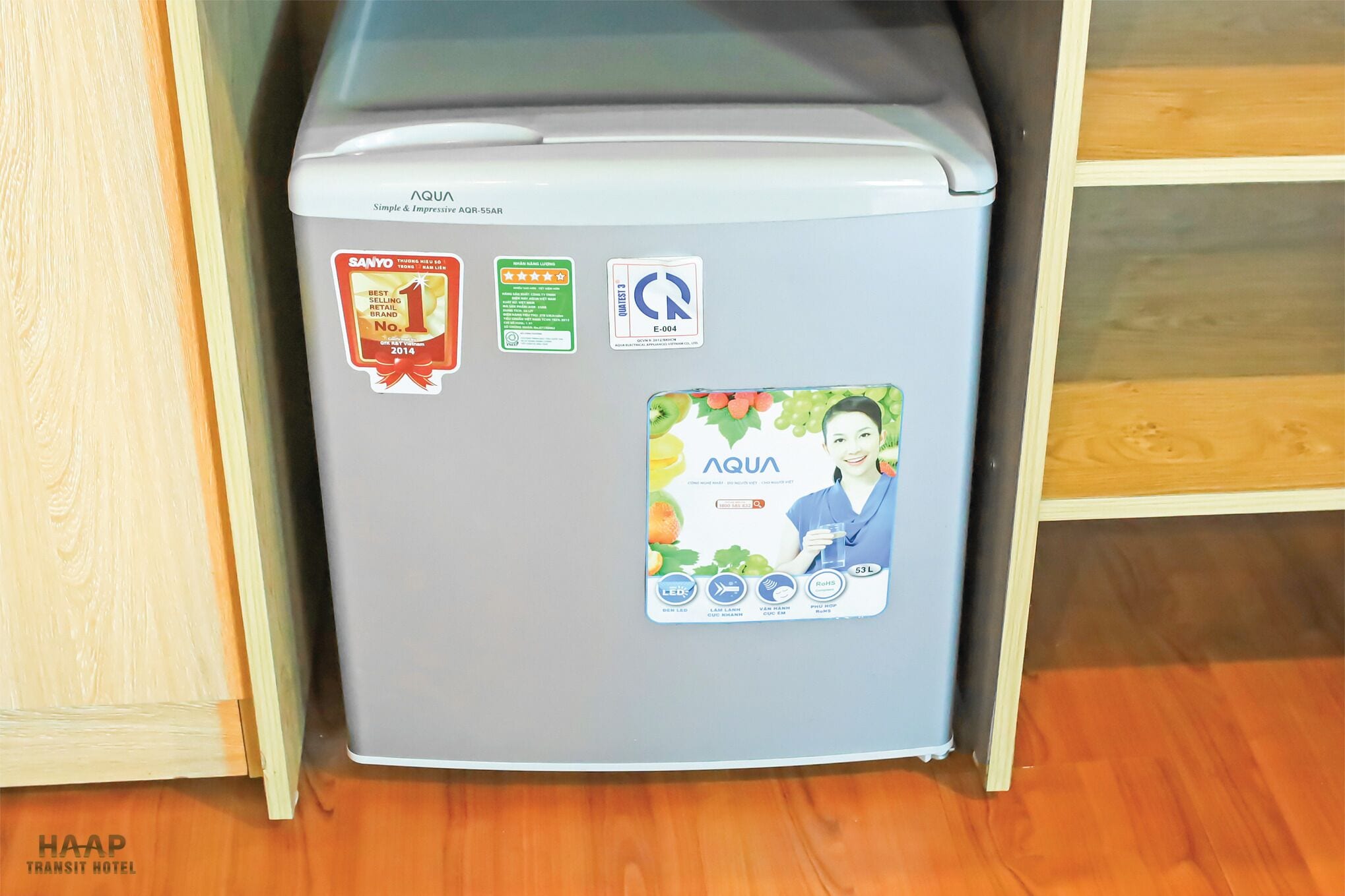 A compact refrigerator with multiple stickers, including a Sanyo award, a green sticker, and a blue sticker with a woman holding a glass.