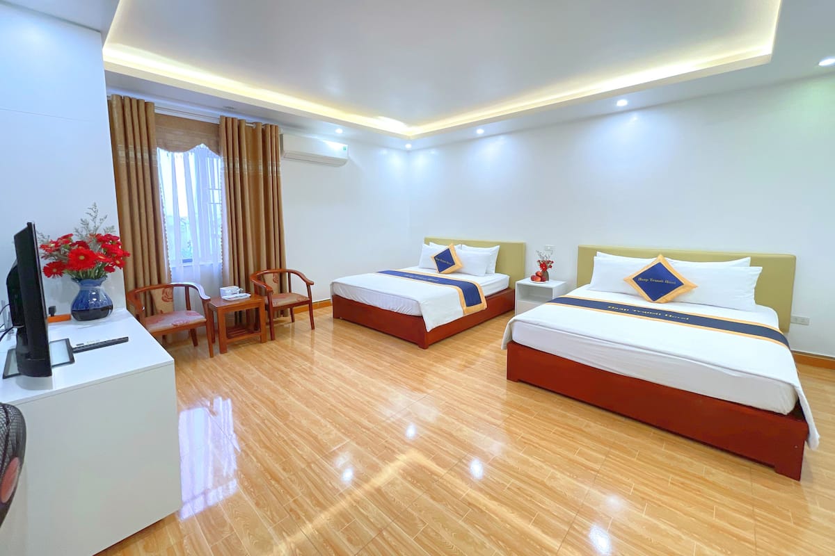 A hotel room with two beds, a desk with a computer, a chair, and a vase with flowers.