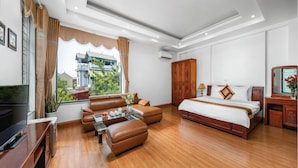 Een moderne hotelkamer met een zithoek, een glazen salontafel, een houten bed en een televisie.