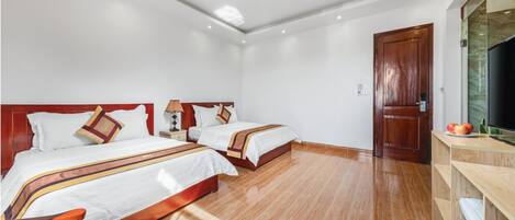 A hotel room with two beds, wooden flooring, a wooden door, and a TV on a wooden cabinet.