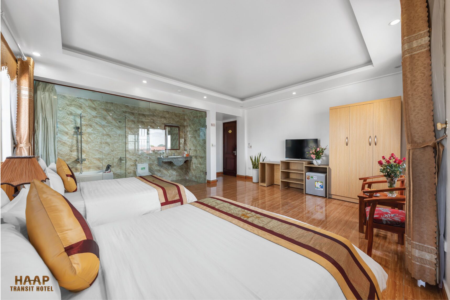 A spacious hotel room with a large bed, a TV, a wardrobe, and a bathroom with a marble wall.