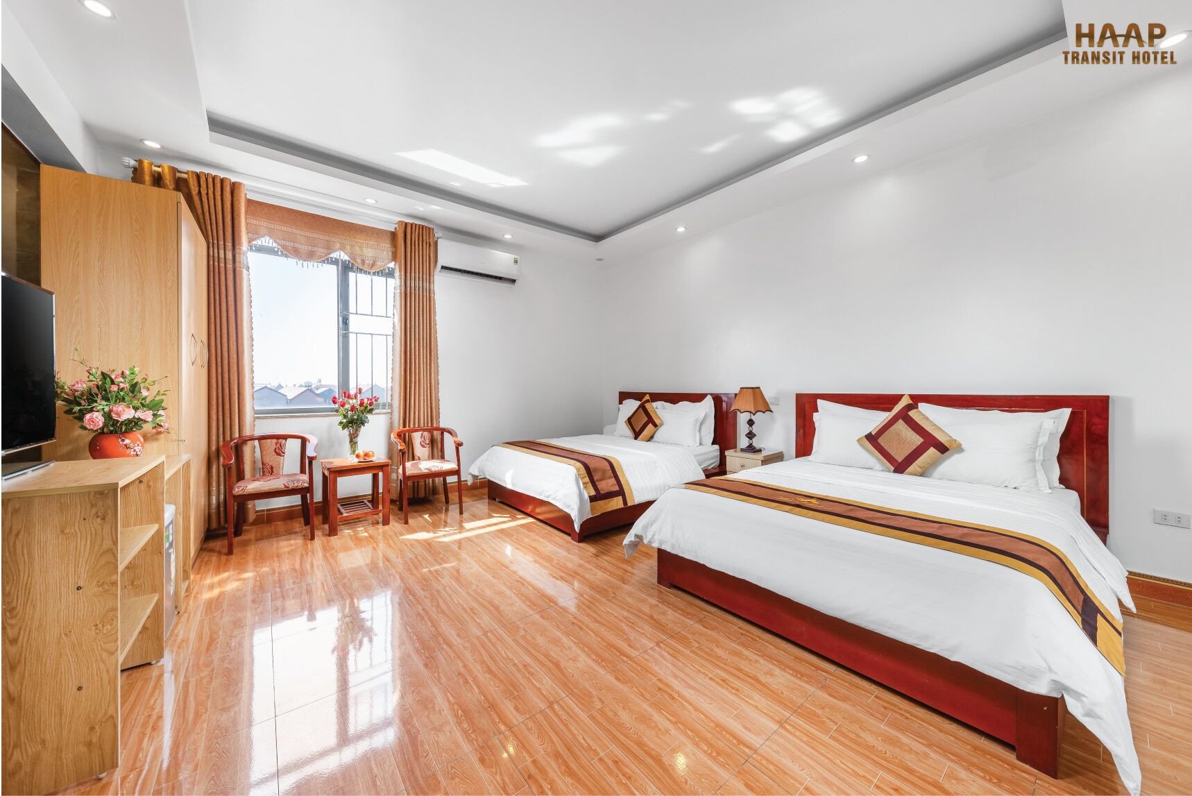 A hotel room with two beds, a TV, a desk, and a window with curtains.