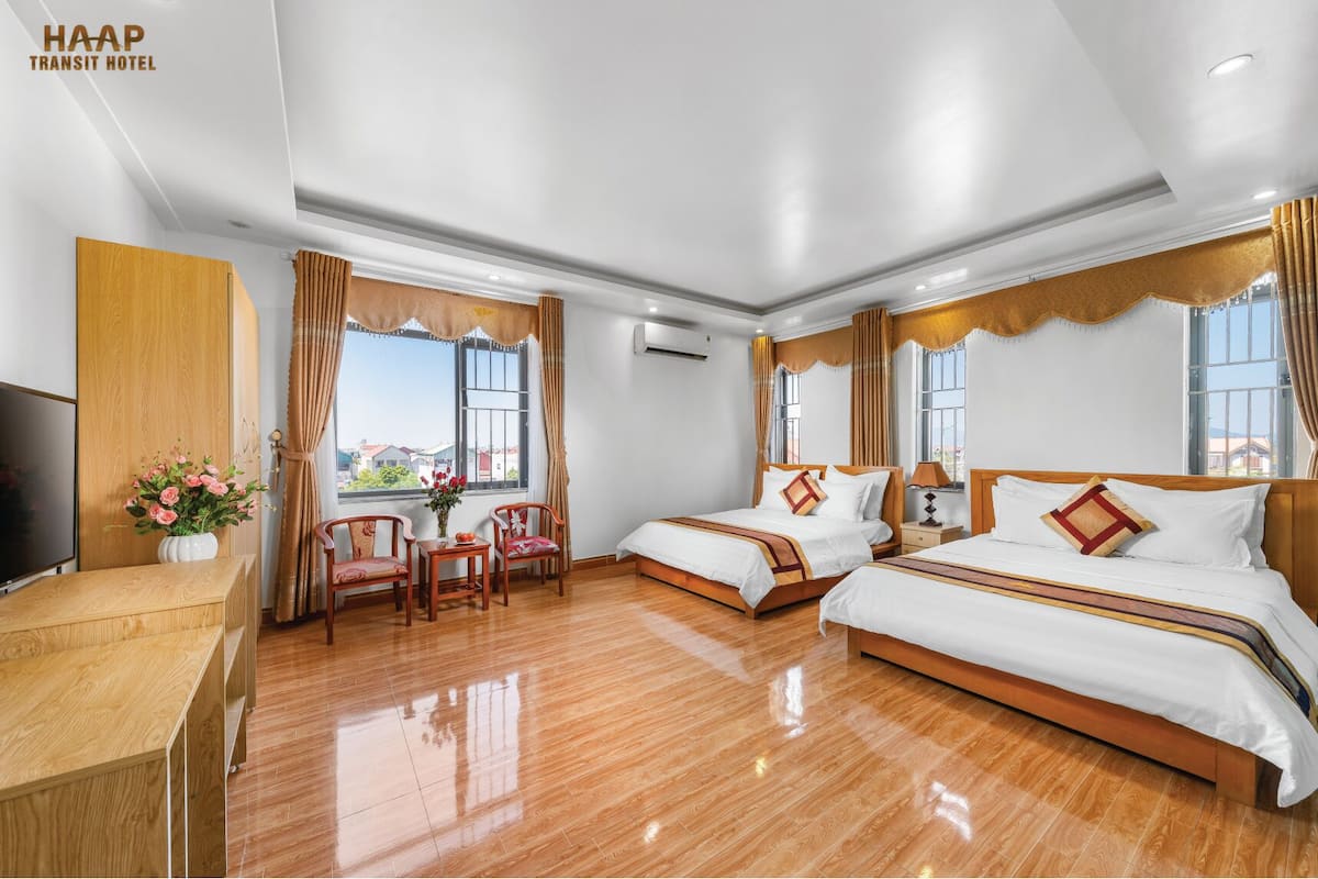 A hotel room with two beds, a wooden desk, a TV, and a view of the city.