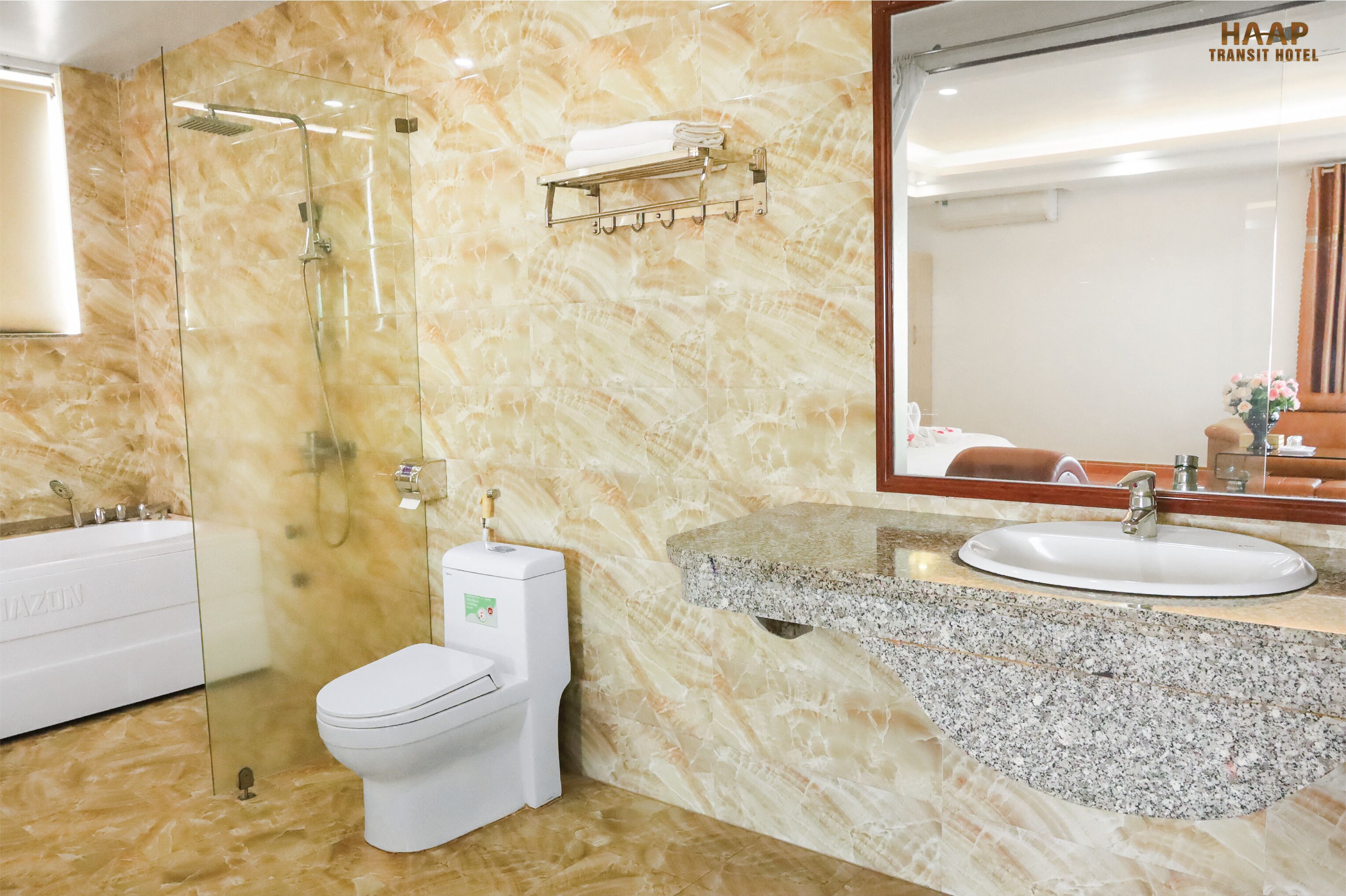 Un baño con pared de mármol, ducha con cerramiento de vidrio, inodoro blanco y lavamanos con espejo.