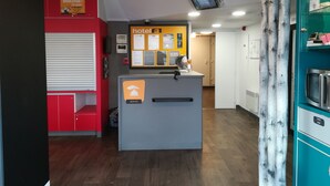 Een hotel receptie met een receptiebalie, een prikbord met mededelingen en een rode muur met een bord.