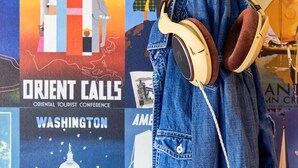 Une paire d’écouteurs posée sur un jean en denim, avec en arrière-plan des affiches de voyage.