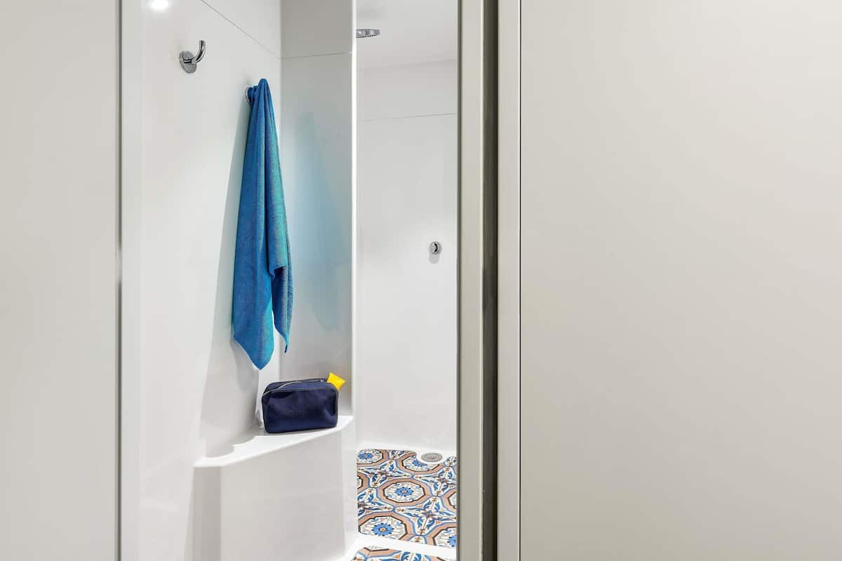 Un baño con pared blanca, una toalla azul colgada en un gancho y un estante con un bolso y un objeto amarillo.