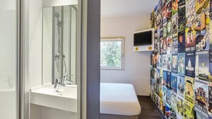 Een badkamer met een douche, een wastafel en een bankje. Een aan de muur bevestigde televisie is zichtbaar.