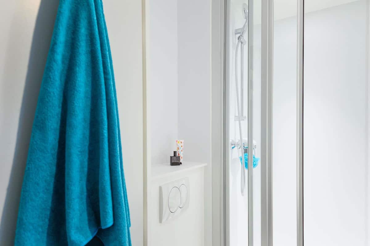 Un baño con cabina de ducha de vidrio, un perchero con una toalla azul y un pequeño estante con artículos de aseo.