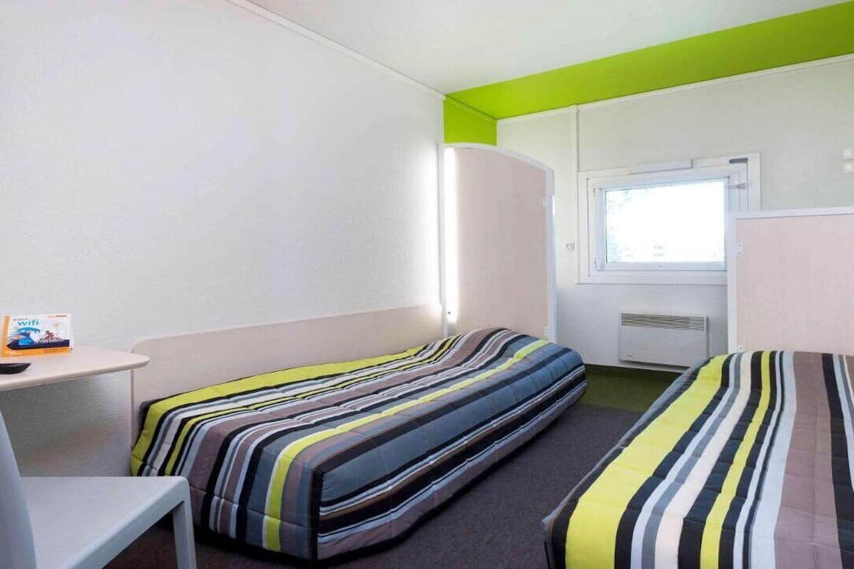 Una habitación pequeña y colorida con dos camas, un escritorio y una ventana.