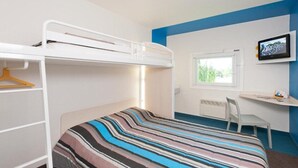 Ein Schlafraum mit Etagenbetten, einer Bettdecke mit Streifenmuster, einem Schreibtisch mit Stuhl und einem Fenster mit Blick auf Grünflächen.