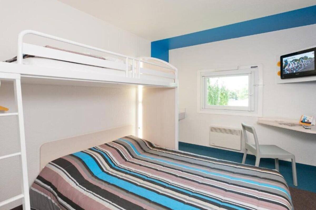 Habitación con literas, colcha a rayas, escritorio con silla y ventana con vista a la vegetación.