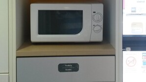 Eine Mikrowelle in einer Küchenzeile mit einem darüberliegenden Regal, das verschiedene Lebensmittel und ein Müllbecken zeigt.