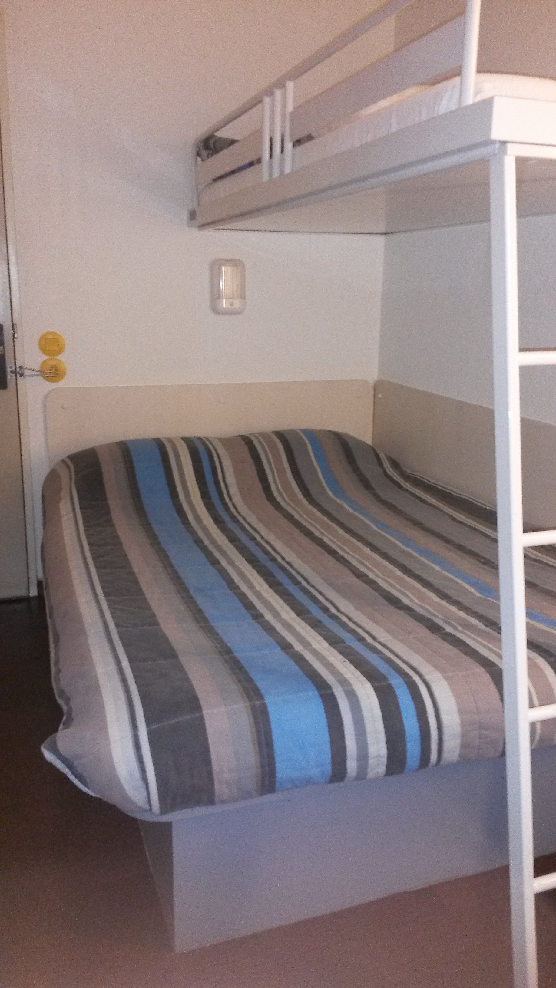 A bunk bed with a striped bedspread, a white wall, and a door with a handle.