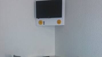 Habitació petita amb un llit, una cadira, un taulell i un televisor fixat a la paret.