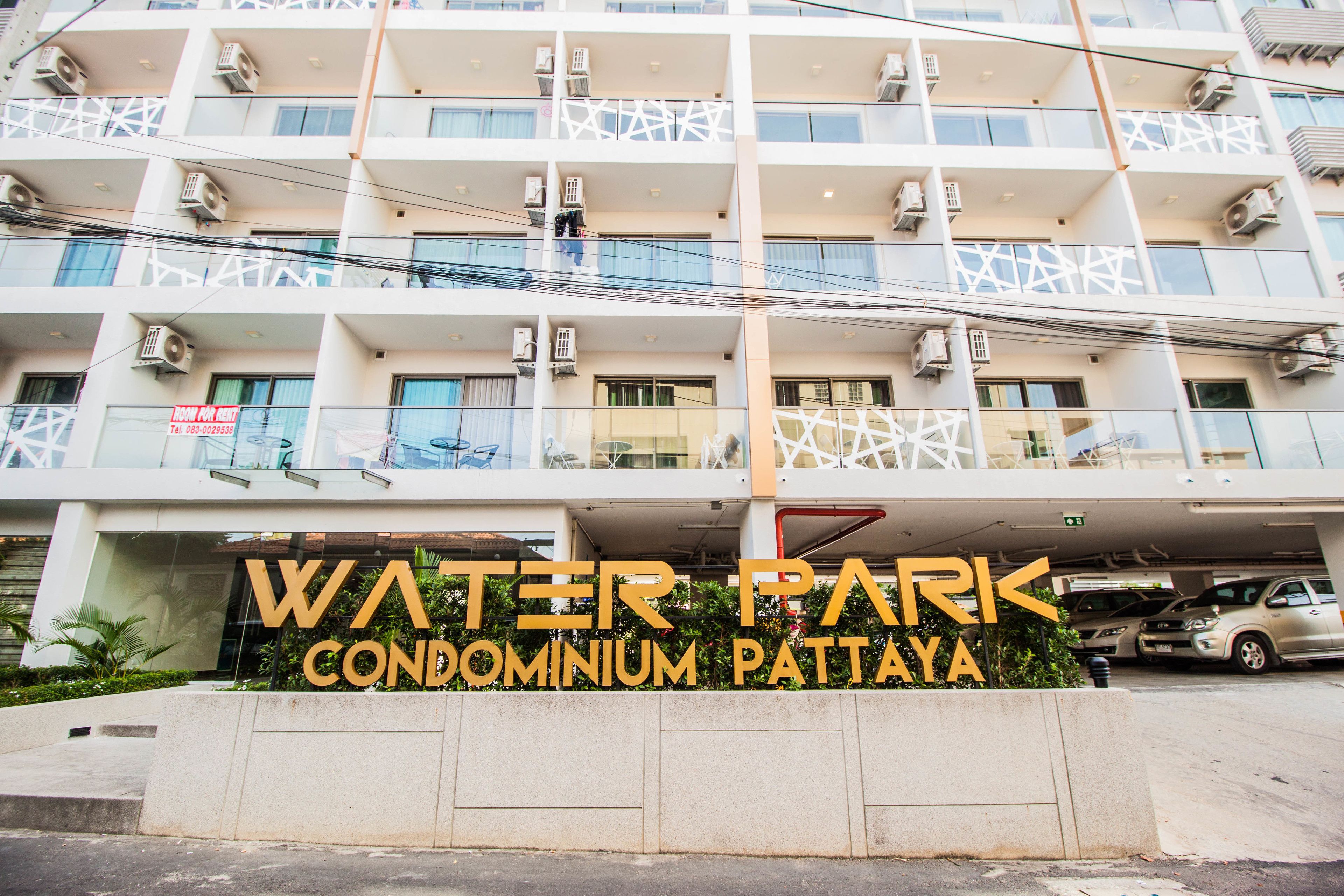 Un edificio de varios pisos con balcones y unidades de aire acondicionado. El letrero dice "Water Park Condominium Pattaya".