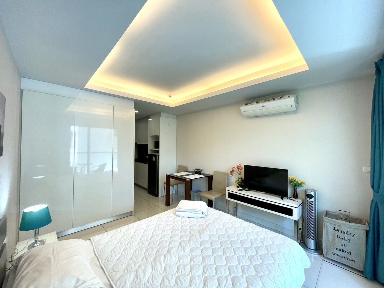 A modern hotel room with a bed, a desk, a TV, and an air conditioning unit.