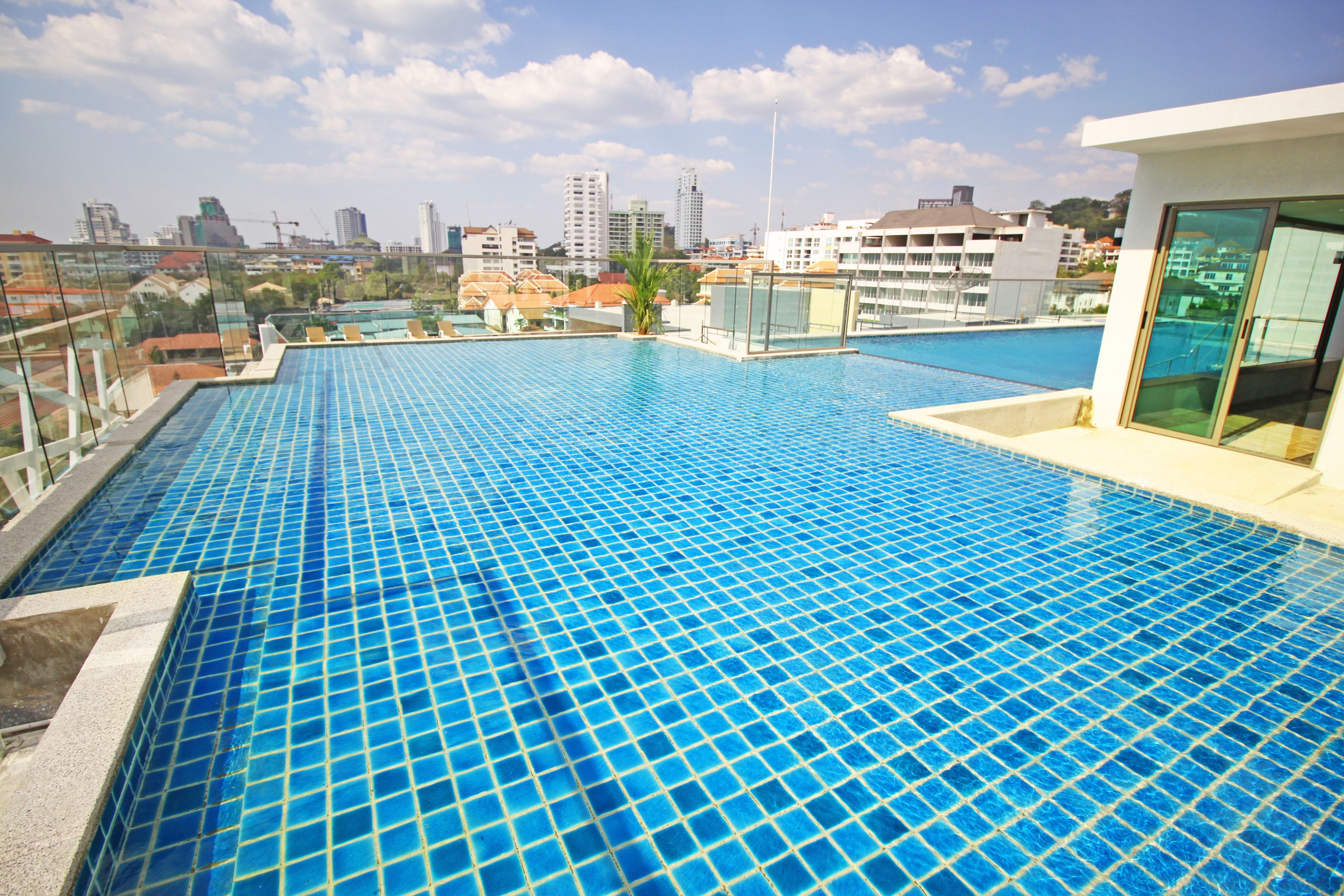 A rooftop infinity pool with a city view, surrounded by glass railings and a modern building structure.