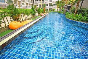 A swimming pool with blue mosaic tiles, surrounded by greenery and a building with balconies. - Water Park by PSR ASIA (Pattaya)