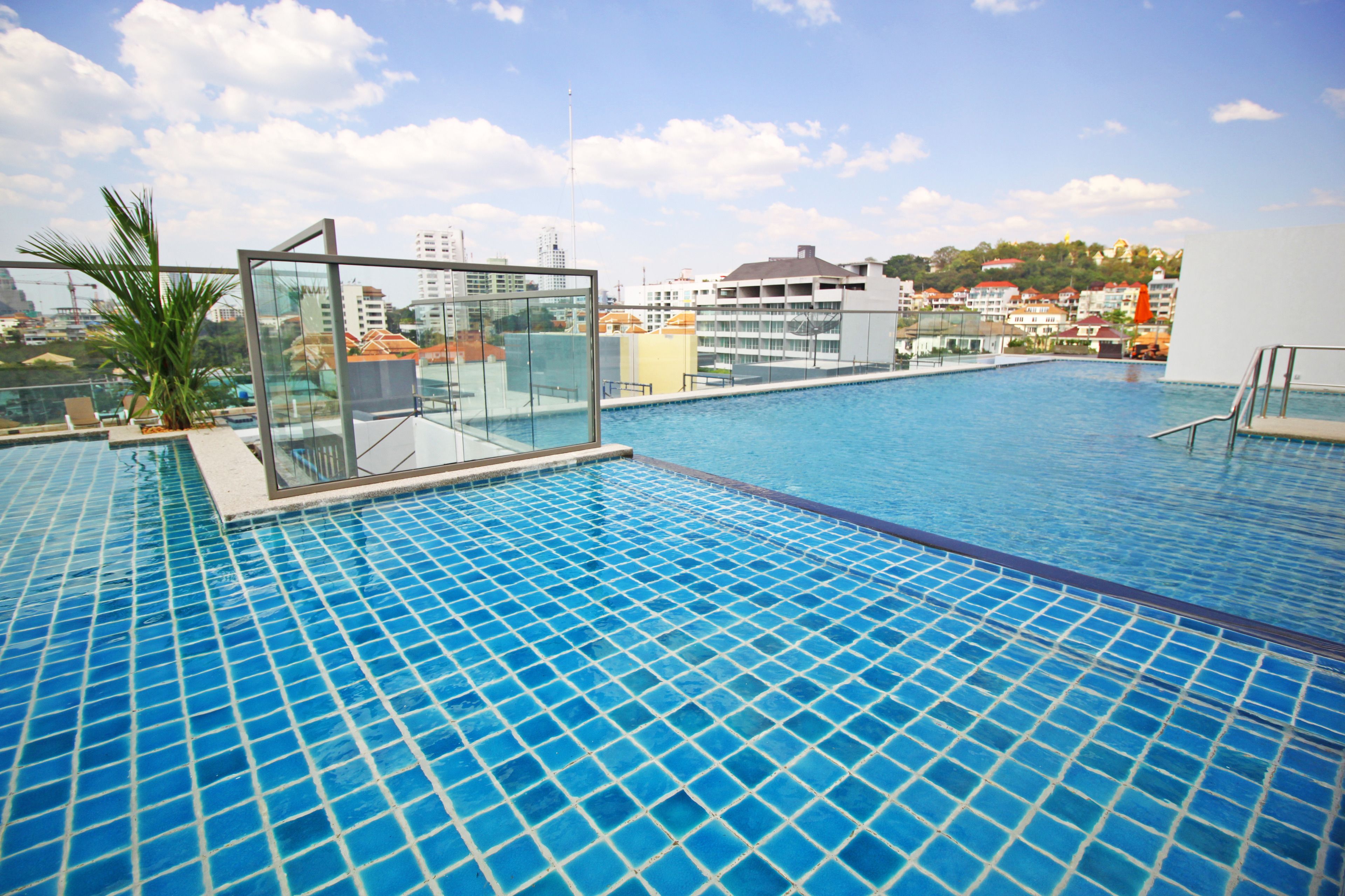 Une piscine à débordement située sur le toit, entourée de parois en verre, avec une vue sur les bâtiments de la ville et un ciel dégagé.