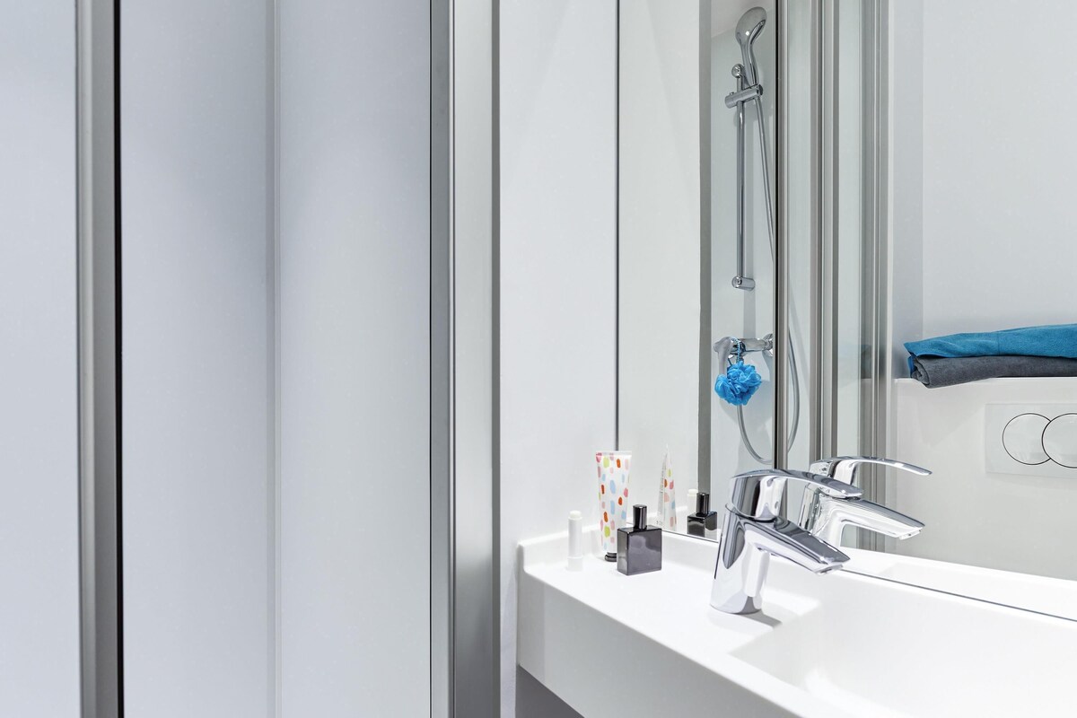 Ein modernes Badezimmer mit einem weißen Waschbecken, einer Duschkabine aus Glas und einem Handtuchhalter mit einem gefalteten Handtuch.