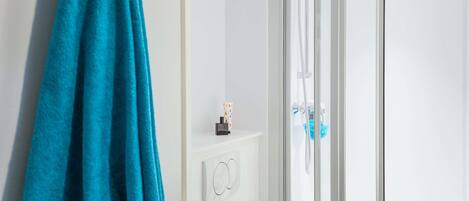 Un baño con cabina de ducha de vidrio, un perchero con una toalla azul y un estante pequeño con artículos de aseo.