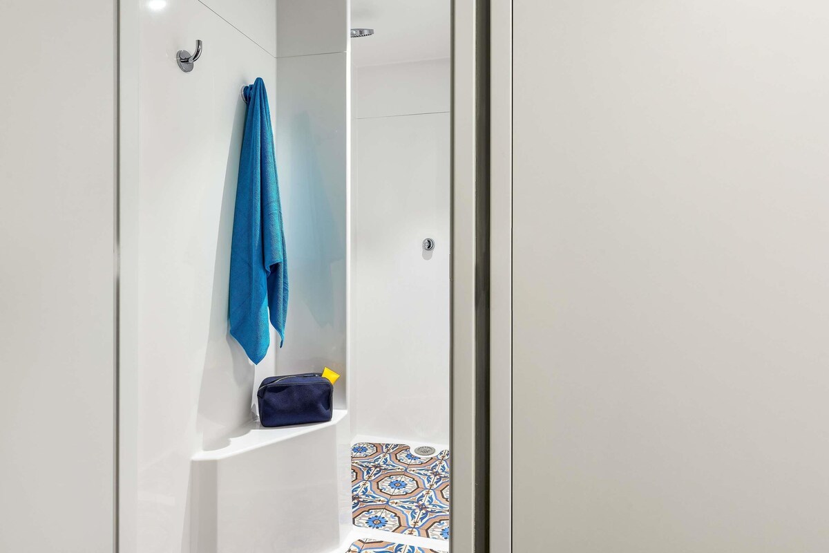 Ein modernes Badezimmer mit Dusche, Handtuchhalter und einer kleinen Ablage mit einer Tasche.