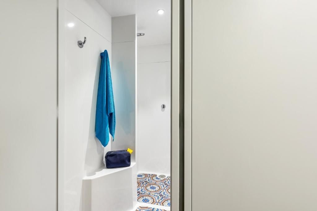 Un baño con cabina de ducha blanca, una toalla azul colgada en la pared y un pequeño estante con una bolsa.