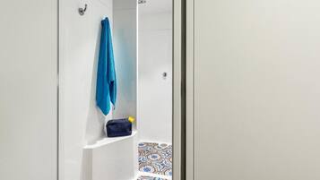 Un baño con cabina de ducha blanca, una toalla azul colgada en la pared y un pequeño estante con una bolsa.