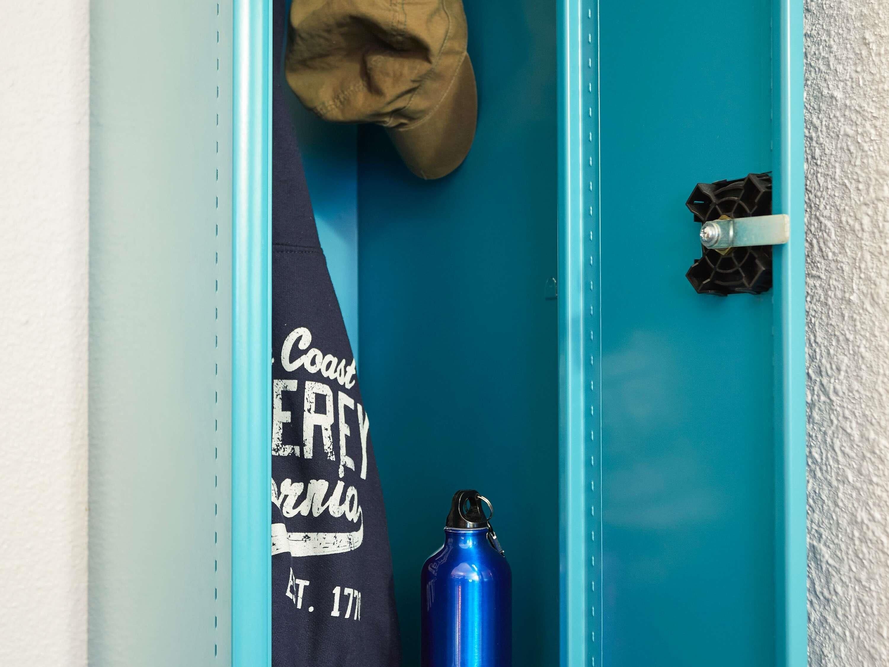 A blue locker with a towel hanging on the door and a blue water bottle inside.