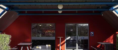 Ein Hotel mit roter Fassade, einem gelben Schild mit der Aufschrift 'hotelFL.com' und einem überdachten Außenbereich mit Tischen und Bänken.
