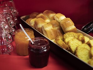 Una bandeja con panecillos y pastelería, un tarro de mermelada y una jarra de vidrio sobre una mesa roja.