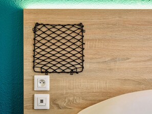 Pared de madera con un estante de malla negra y dos enchufes.