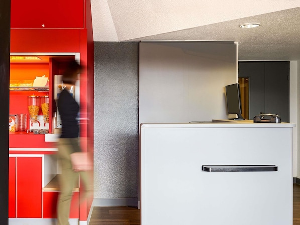 A modern interior with a red counter, a white reception desk, and a textured grey wall.