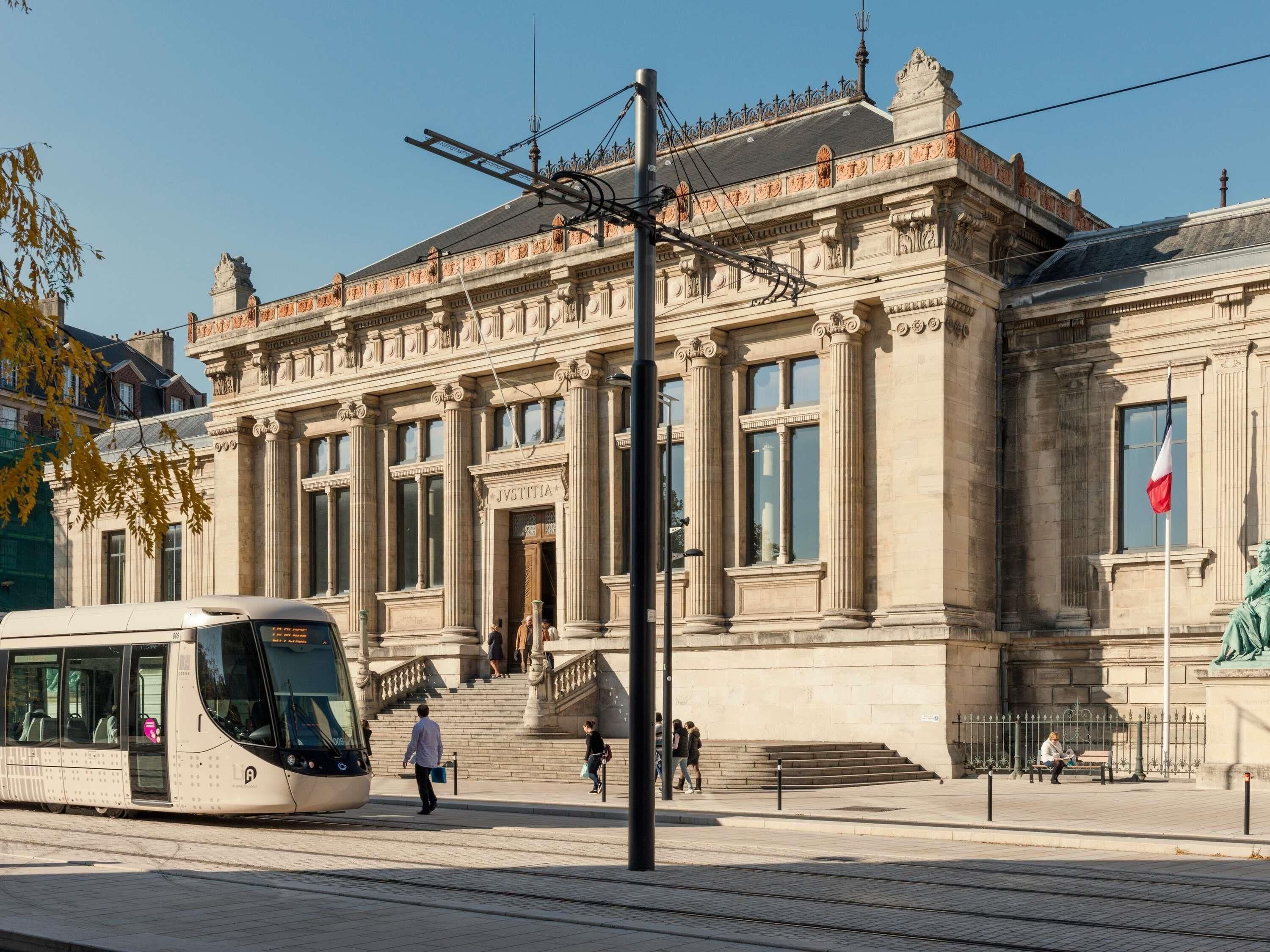 A historic building with classical architecture, a tram, and people walking.