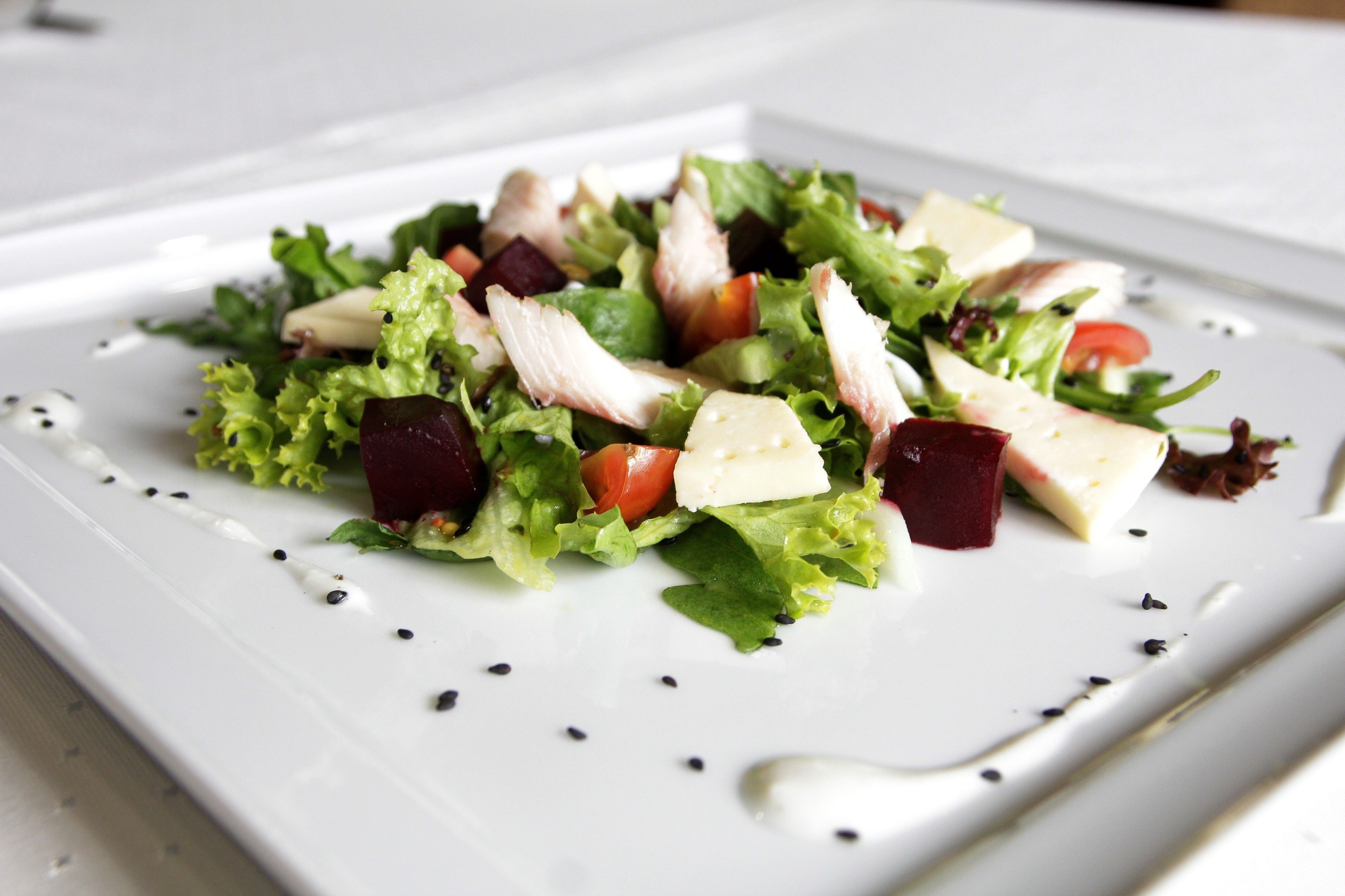 A white rectangular plate with a salad consisting of lettuce, tomatoes, beets, and cheese, accompanied by a spoon.