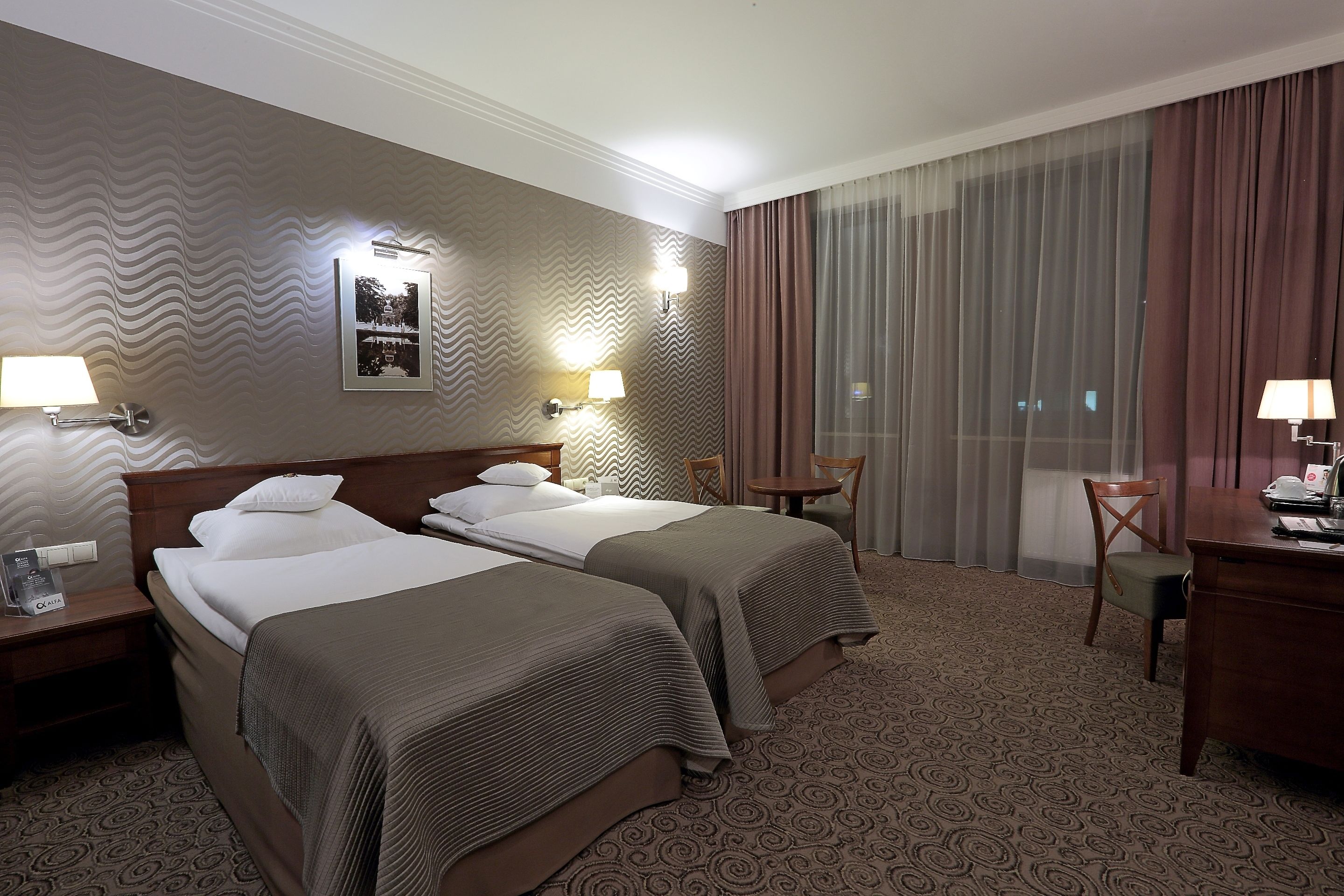 Habitación de hotel con dos camas, un escritorio, una silla y un ventanal con cortinas.