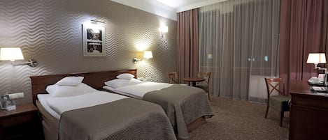 Habitación de hotel con dos camas, un escritorio, una silla y un ventanal con cortinas.