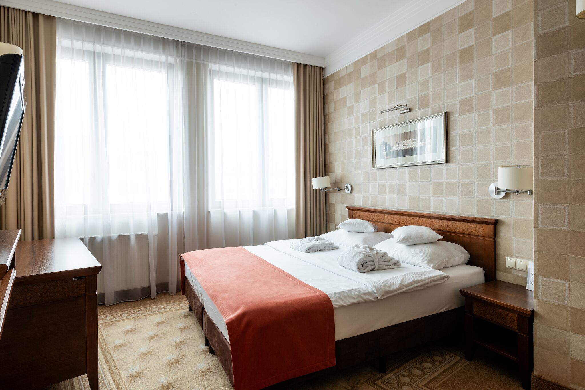 A hotel room with a bed, a desk, a TV, and a window with curtains.