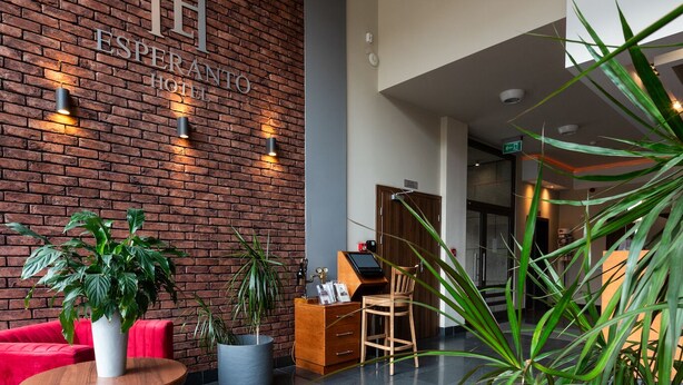 Un moderno vestíbulo de hotel con asientos rojos, plantas en macetas y una pared de ladrillo con el nombre del hotel.